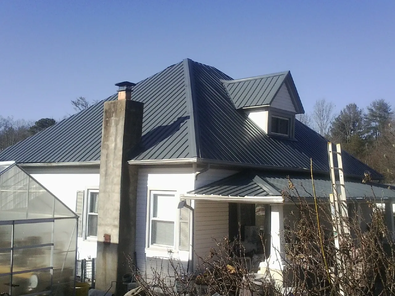 Dark blue standing seam metal roof on a white farmhouse with dormer — Slate & Tile Roof Repair by Roofing Brothers in Balaton