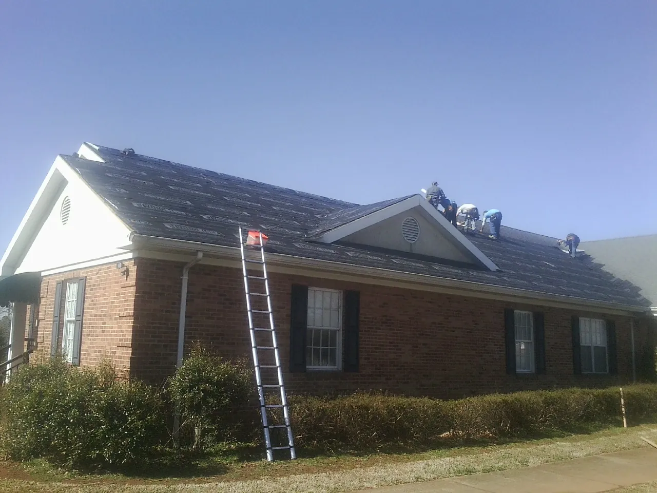 Crew tearing shingles off a brick ranch roof with a ladder set — Emergency Roof Repair work by our crew in Balaton