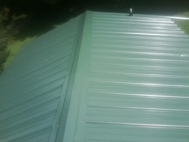 New green metal panels meeting at the ridge of a roof — Flat Roof Repair work by our crew in Balaton