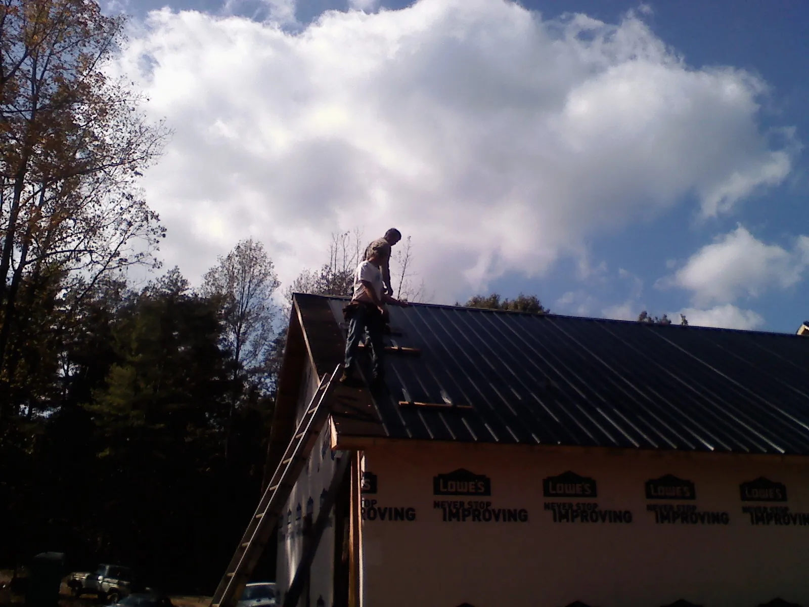 Roofer fastening dark metal panels high against a cloudy sky, from a Roof Inspection job in Balaton
