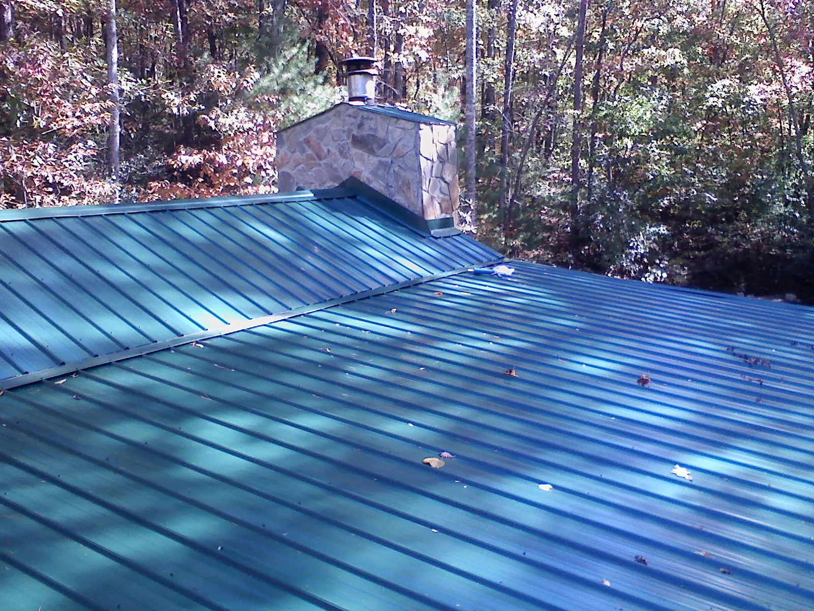 New green metal roof and stone chimney surrounded by autumn woods in Balaton